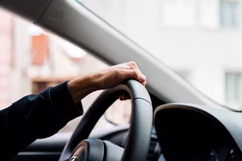 Gros plan sur la main d’un conducteur tenant le volant d’un véhicule en mouvement.